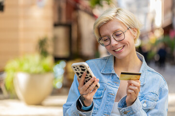 Smiling young woman using credit bank card smartphone while transferring money, purchases online...