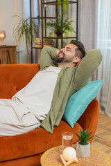 Tired Caucasian handsome man enjoy relaxing on home sofa in living room. Happy guy lying on couch...