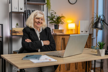 Senior businesswoman closing laptop after finishing work at home office desk. Smiling female...