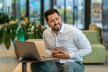 Disappointed Caucasian young man feeling overeating during work process on laptop in modern office...