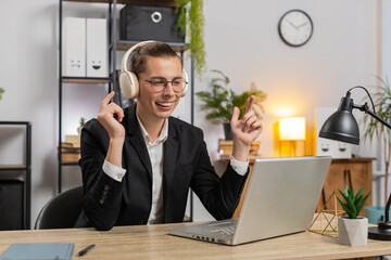 Happy young businessman wears wireless headphones having fun listening music. Smiling employee...
