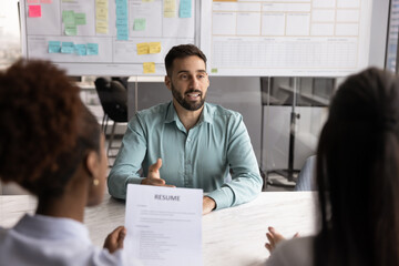Hispanic male applicant answers questions, speaking about education, work experience, professional skills and accomplishments, passing job interview sit in front of two HR managers in company office