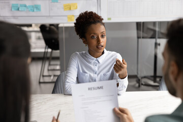 Young African woman answers questions during job interview meeting with two HR managers listening...