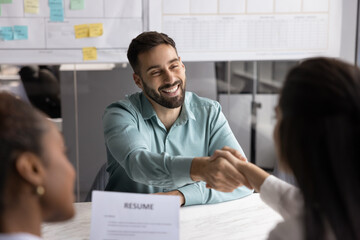 Happy Hispanic man shaking hands with female HR manager or employer seated at table in meeting...