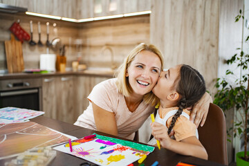 Cute girl kisses her mother while they both work on vibrant art projects