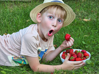 Portrait of a boy aged 6-7 with strawberries and strong emotions. Boy eating strawberries in the garden.