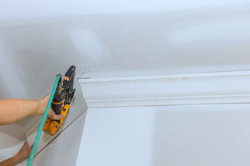 Carpenter is installing crown molding in contemporary room using power tool for pneumatic nail gun