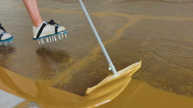 Closeup footage of a worker spreading epoxy resin smoothly across a floor with a large squeegee tool