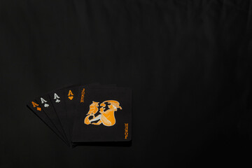 A hand of cards featuring four aces and a joker card on a dark black background surface spread out