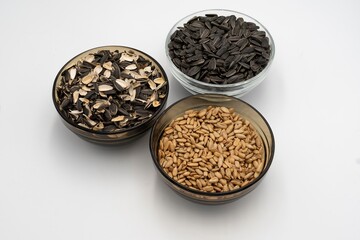 Three transparent bowls with sunflower seeds and husks: raw, peeled and husk on a white background