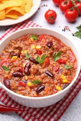Tasty chili con carne in bowl, nachos and ingredients on grey table, closeup