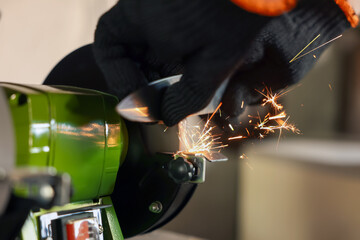 Man sharpening knife with bench grinder indoors, closeup