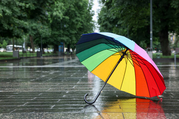 Colorful umbrella on wet asphalt outdoors, space for text