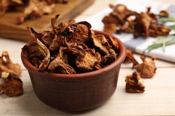 Dried chanterelle mushrooms in bowl on light wooden table, closeup