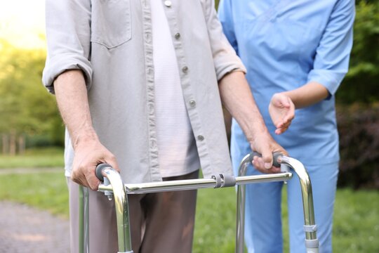 Nurse helping elderly man who using walking frame outdoors, closeup