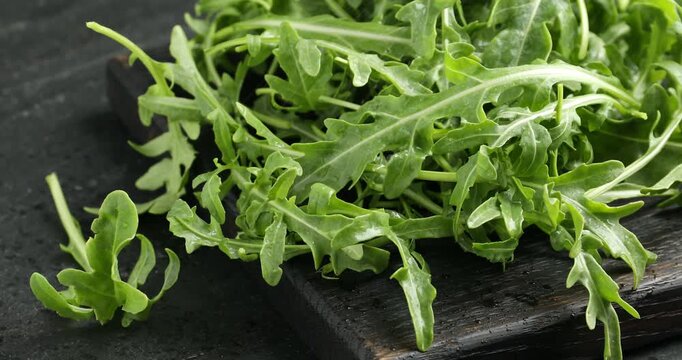 Spraying water onto fresh ripe green arugula leaves on black table, closeup