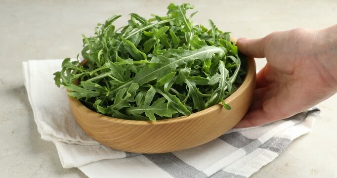 Woman putting fresh ripe green arugula leaves on white table, closeup