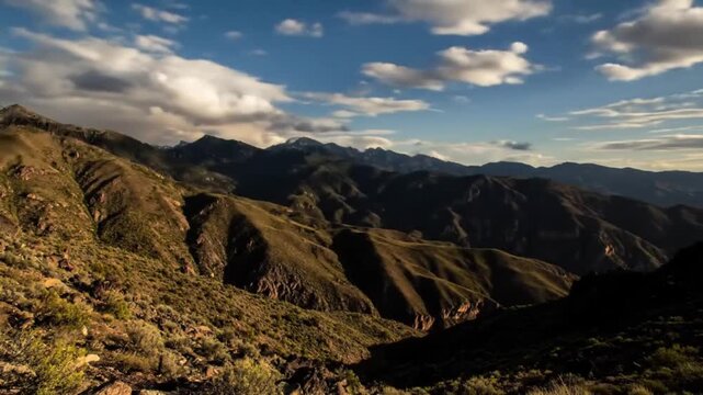 High-speed time-lapse of dramatic clouds rolling over mountains during golden hour, shadows shifting across the terrain