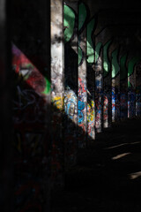 Fototapeta premium Graffiti-covered concrete pillars in abandoned underpass with dramatic light