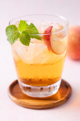 Iced peach tea with fresh sliced peaches and mint leaf in glass on pink background, Summer drink