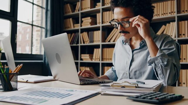 Financial Economist Using Calculator to Manage Accounts Payable, Receivable, and Taxes in Casual Office Setting