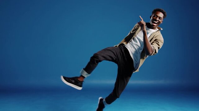 An energetic young man jumping excitedly against blue backdrop, pointing toward blank space for promotional use