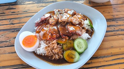 Red pork and crispy pork on rice in a blue plate on a wooden table