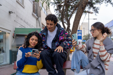Young latin american friends using smartphones on city bench