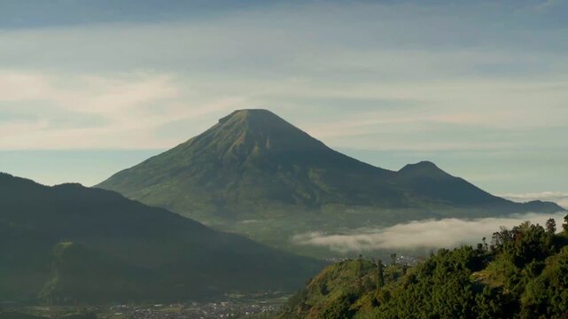 A breathtaking view featuring a prominent volcanic mountain surrounded by green hills under a vast blue sky.