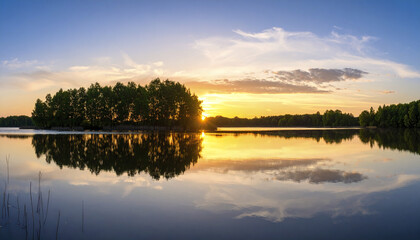 Obraz premium Sunrise over calm lake with silhouetted trees reflecting on gentle water surface creating peaceful and serene natural landscape scene