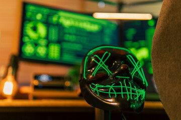 In a dimly lit cyber lair, a glowing hacker mask watches over a desk as encrypted code streams...