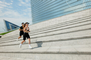 Fototapeta premium Energetic joggers racing up modern stairs under a sunny urban sky