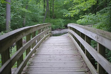 Fototapeta premium A wooden bridge over the creek in Cuyahoga Valley National Park, surrounded by lush greenery and trees. The focus is on one side of the wooden walkway leading to an unseen destination.