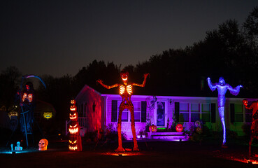Halloween night house exterior with spooky decor. Scary skeleton in front yard. Home decorated with...