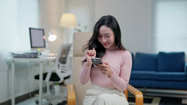 Cheerful freelancer working remotely on smartphone, sitting comfortably in home workspace with relaxed demeanor and natural lighting
