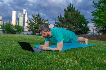 Online fitness. Online workout on yoga mat outdoor. Mature man training with online fitness video....
