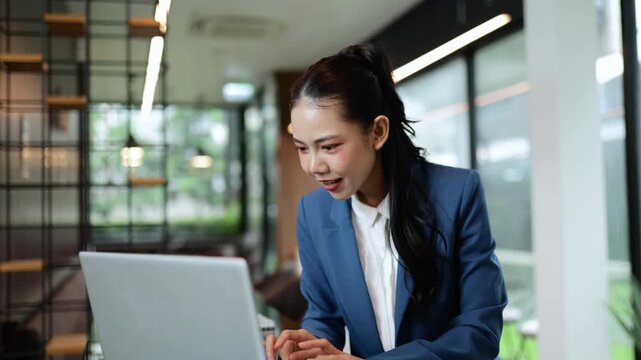 Professional businesswoman experiencing multiple positive emotions while working on laptop, showcasing success and joy in modern, bright office environment with natural window light