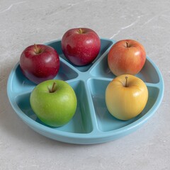 Assorted fresh apples in a colorful divided plastic tray on a neutral surface, showcasing vibrant red, yellow, and green varieties for healthy eating or food presentation