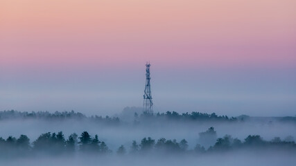 Cell tower emerging from fog at dawn