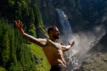 Man Meditation and wellness in nature. Freedom in environment. Relaxed man meditating against waterfall at forest in nature. Freedom and happiness lifestyle. Wellness spa vacation and yoga meditation.