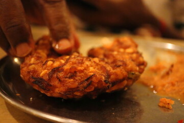 Close-Up of South Indian Masala Vadai Being Picked by Hand – Authentic Street Food Scene with Rich Texture and Flavor – Crispy Traditional Snack from Tamil Nadu