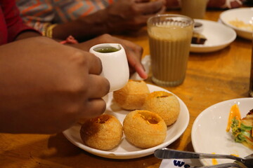 Close-up of Indian street food Pani Puri being filled with tangy spicy water, served with masala chai in a traditional dining setting – authentic Indian snacks and tea experience