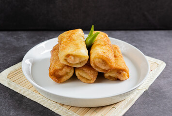 Sosis Solo (Sausage Solo). Special designation for a chicken dish wrapped in an omelet and shape like sausagea. Traditional Indonesian meat snack, served on a white plate with green chili garnish.