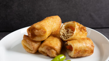 Close up Sosis Solo (Sausage Solo). Special designation for a chicken dish wrapped in an omelet and shape like sausagea. Traditional Indonesian snack, served on a white plate with green chili garnish.