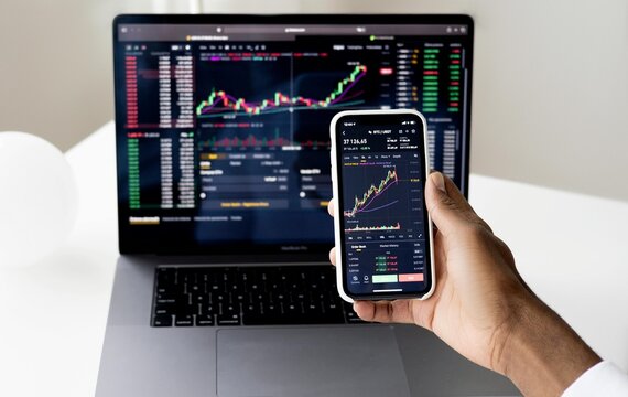 Businessman checking stock market on digital tablet and a desktop computer with stock exchange graph on screen. Financial stock market. Analyzing data in office background.