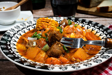 Fork picking up beef stew called carbonada with butternut squash, corn on the cob, and carrots