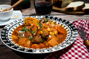 Delicious beef stew called carbonada with corn on the cob, vegetables, and red wine