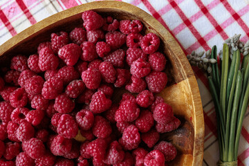 On a rustic tablecloth stands a wooden bowl with ripe raspberries and a bouquet of muscari lies nearby.
