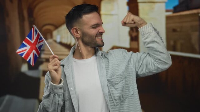 Hispanic young man on university campus joyfully holds uk flag and flexes arm in celebration.