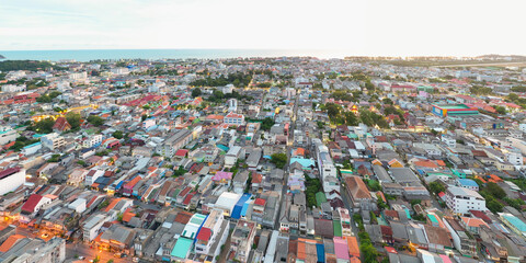 Aerial view of Songkhla city, Thailand, showcasing a vibrant tapestry of rooftops stretching towards the distant coastline under a soft sky.